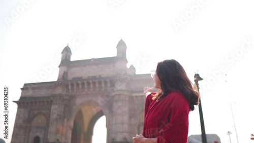 Portrait of smiling Indian girl showing Gateway of India in Mumbai, India. Welcoming gesture of girl. Indian girl background. Beautiful smiling confident young Indian ethnic woman. photo