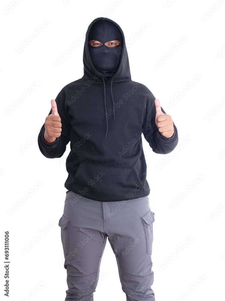 An unidentified male criminal wearing a black hoodie and covering his face stands with a thumbs up. On a white background with cliping path. Thief.weapon, crime.