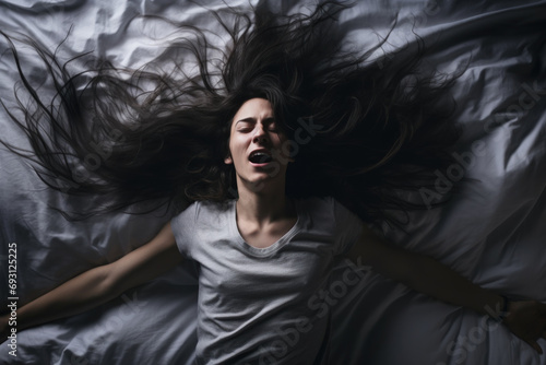 A woman in bed with her hair down in a crazy energetic manner in the bedroom against the night lights has an exaggerated expression of fear, irritability.