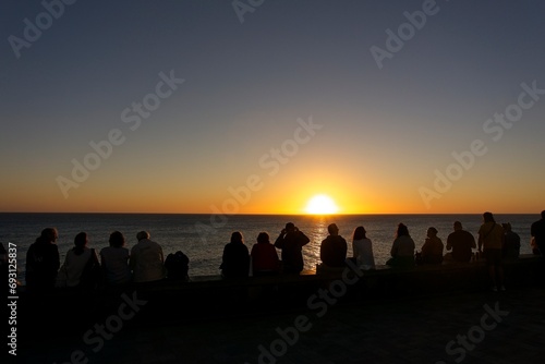Rear view of a group of people silhouette on the beach at sunset against sun in Maspalomas, Gran Canaria, Spain photo