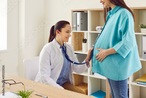 Pregnancy checkup. Female obstetrician examines pregnant woman's abdomen with stethoscope in maternity hospital. Gynecologist listens to heartbeat of baby in woman in last stages of pregnancy.