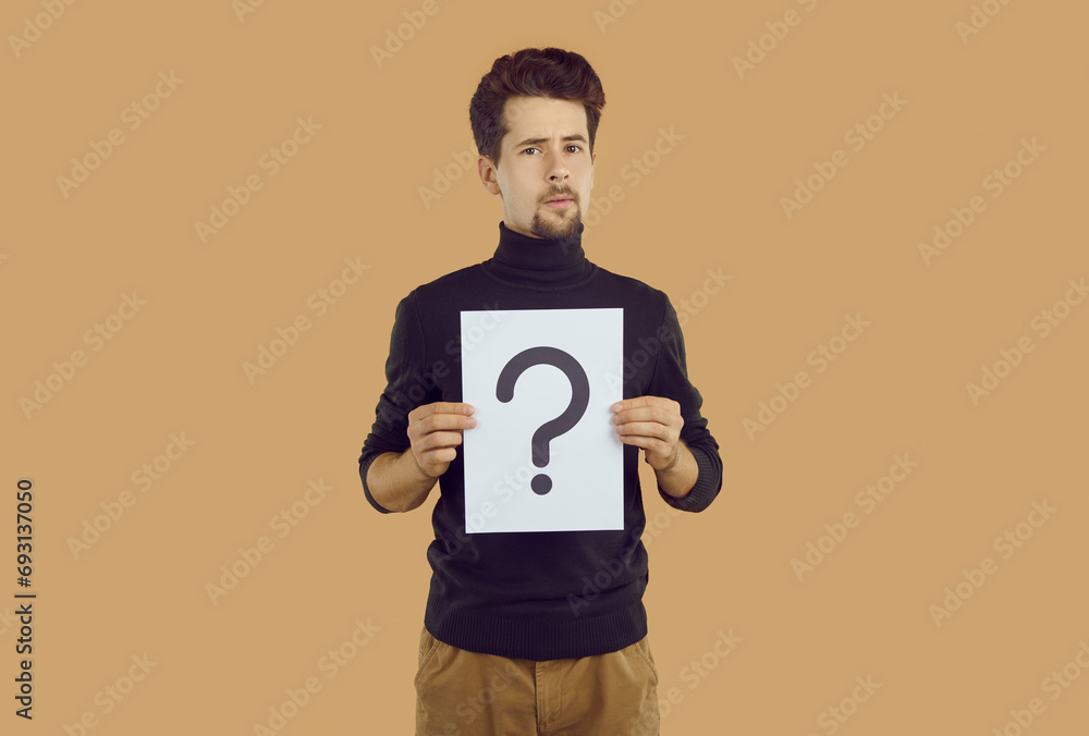 Doubting young man holding paper note with question mark. Portrait of puzzled thoughtful guy wearing casual style clothing showing question sign trying to solution problems, getting answers Doubting young man holding paper note with question mark. Portrait of puzzled thoughtful guy wearing casual style clothing showing question sign trying to solution problems, getting answers