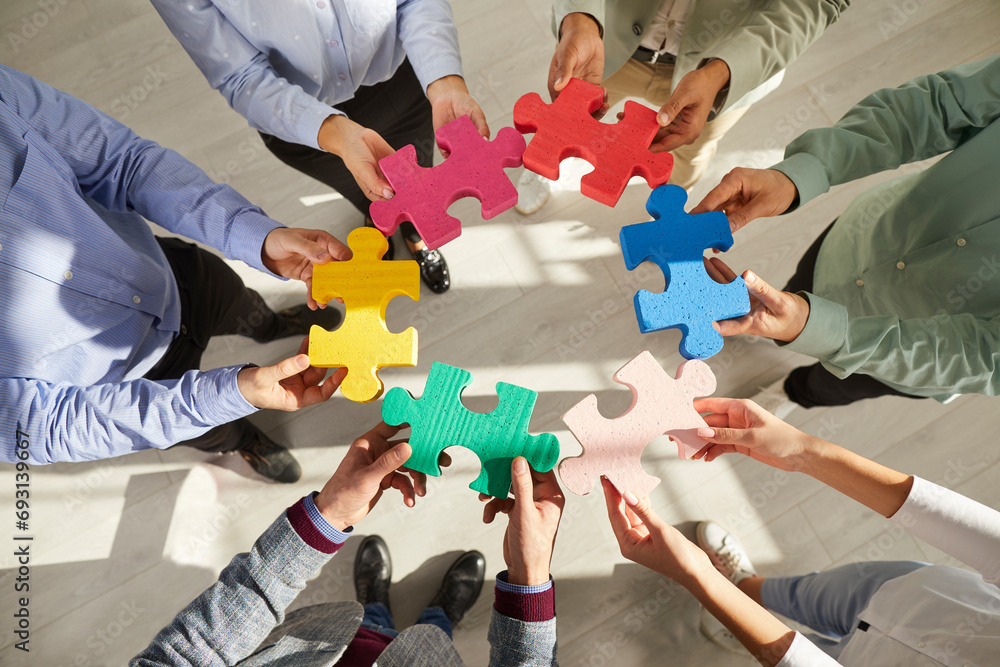 Business team playing with puzzle. Group of young people connecting green, yellow, pink, red, blue pieces of jigsaw puzzle. People holding different jigsaw parts in hands. Teamwork concept background - obrazy, fototapety, plakaty 