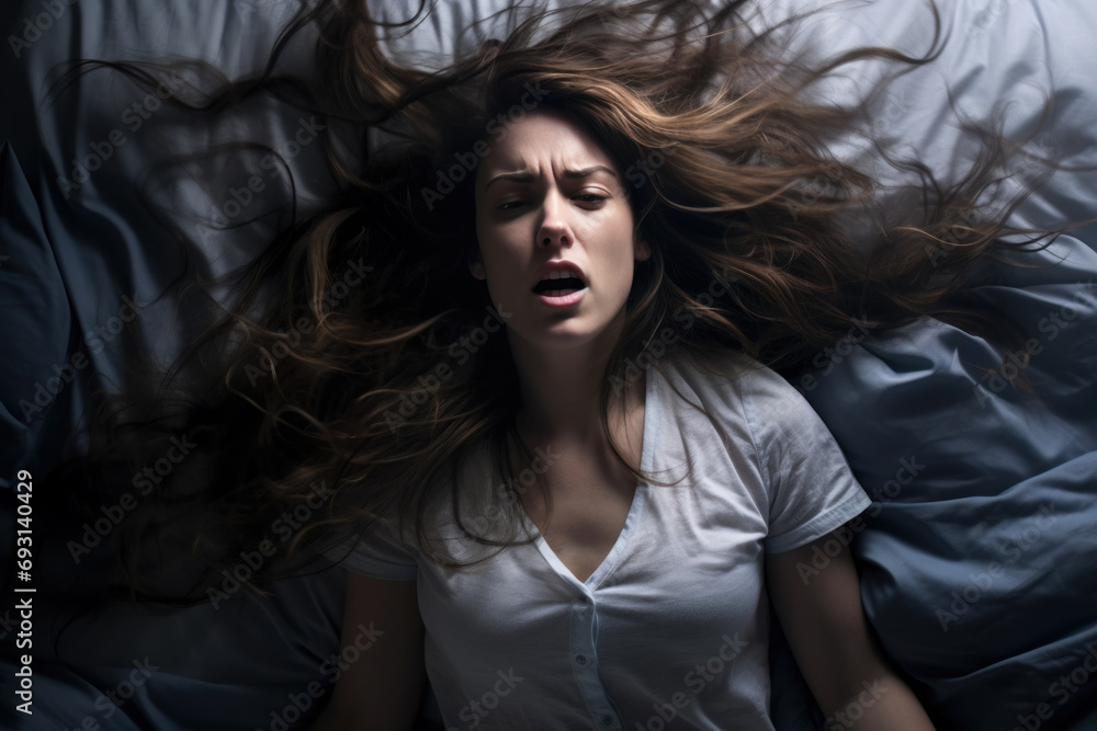 A woman in bed with her hair down in a crazy energetic manner in the bedroom against the night lights has an exaggerated expression of fear, irritability. - obrazy, fototapety, plakaty 
