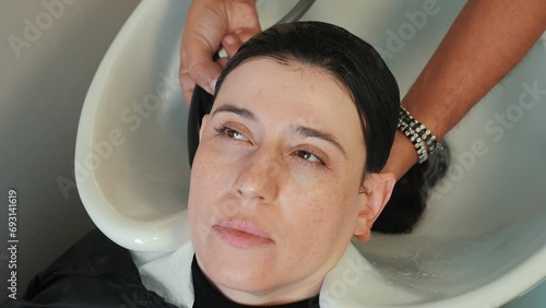 Shampoo rinsed from young woman's dark hair at salon wash station. The hairdresser rinses the shampoo from the hair. The stylist rinses the shampoo lather from the client's head. Training at the hair photo
