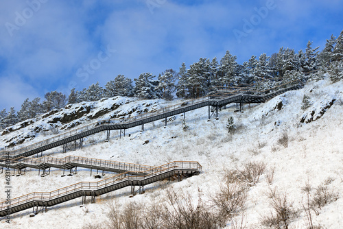 Walking staircase on a snowy hillside in sunny winter day at Krasnoyarsk, Russia. Empty long staircase against snowy pine trees and blue sky.