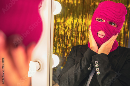 A young woman in a pink balaclava looks in the mirror