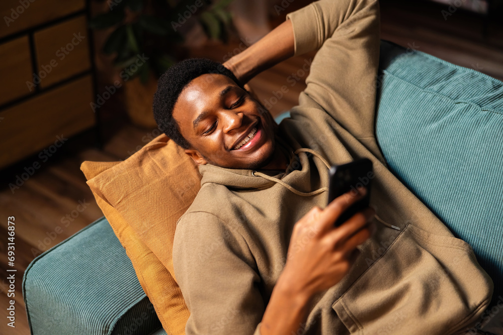 Fototapeta premium Happy delighted cute handsome African American dark skinned businessman taking a phone call in the comfort of his home.