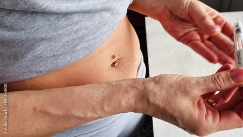 Close up footage of the woman with beautiful hands, preparing hormone medicine and injecting herself to the abdomen with pierced bellybutton. Family planning photo
