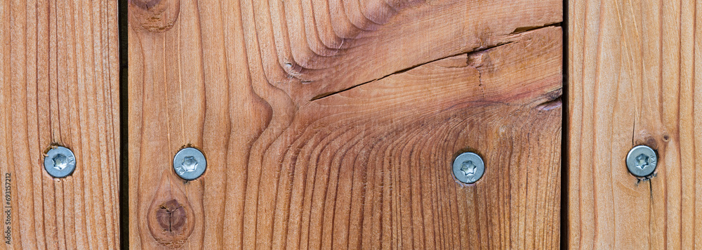 Closeup of larch boards and steel wood screws in wooden panoramic background. Paneling detail of natural planks with narrow slits, a crack and stainless self-drilling torx woodscrews in brown texture. - obrazy, fototapety, plakaty 