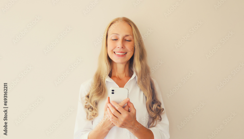 Portrait of happy smiling middle-aged caucasian woman looking at mobile phone on beige studio background Portrait of happy smiling middle-aged caucasian woman looking at mobile phone on beige studio background