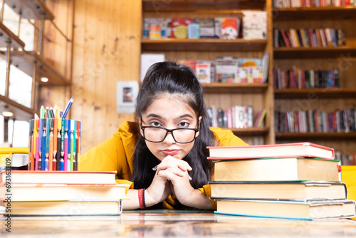 A beautiful young girl business woman or student wearing glasses spectacles of eyeglass seating with pile of books working studying in school collage library or in corporate office sitting with books