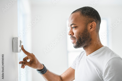 man choosing temperature on thermostat. Young focused guy pushing button home system.