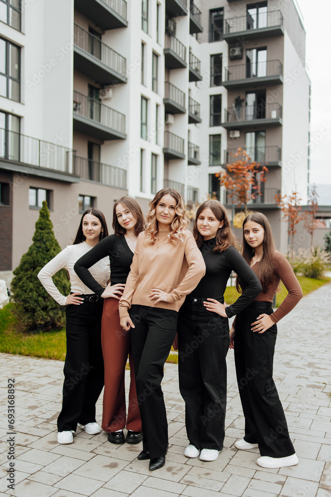 Fototapeta premium Group of smiling and happy teenage friends wearing casual clothes spending time together, posing and talking with each other near college building on autumn day.