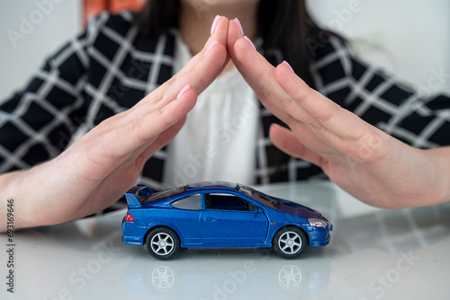 Small blue toy car and female hand at office desk as insurance