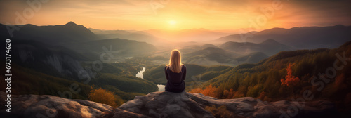 Fototapeta Young woman sitting on a ledge of a mountain and enjoying the beautiful sunset over a wide valley