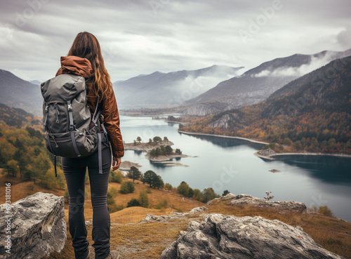 back view of woman hiker with backpack standing on edge of cliff against background of sunset and looking ahead