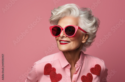Photographie mujer senior portando gafas rojas y camisa rosa con corazones rojos, sobre fondo