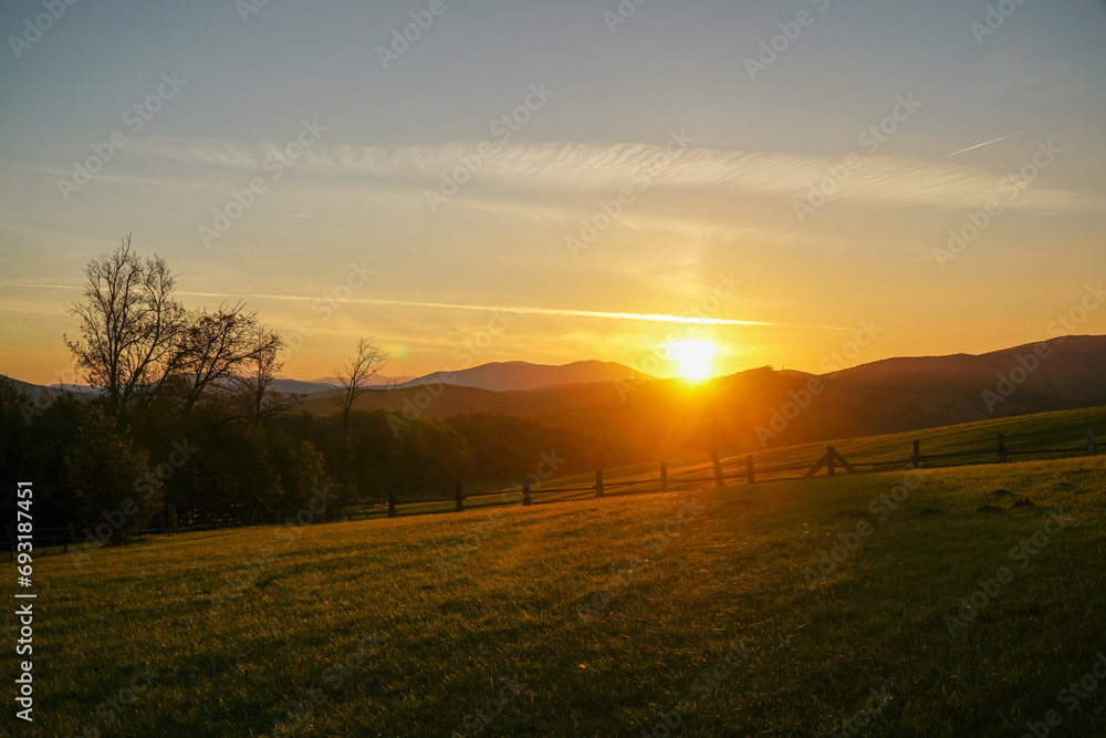 Obraz premium Idyllic colorful sunset scenery at Hochroterd in Breitenfurt in autumn. View to green meadow and rolling hills in the background in Lower Austria.