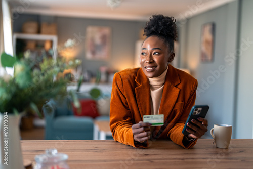 Beautiful African businesswoman sitting at home office using smart phone and credit card. photo