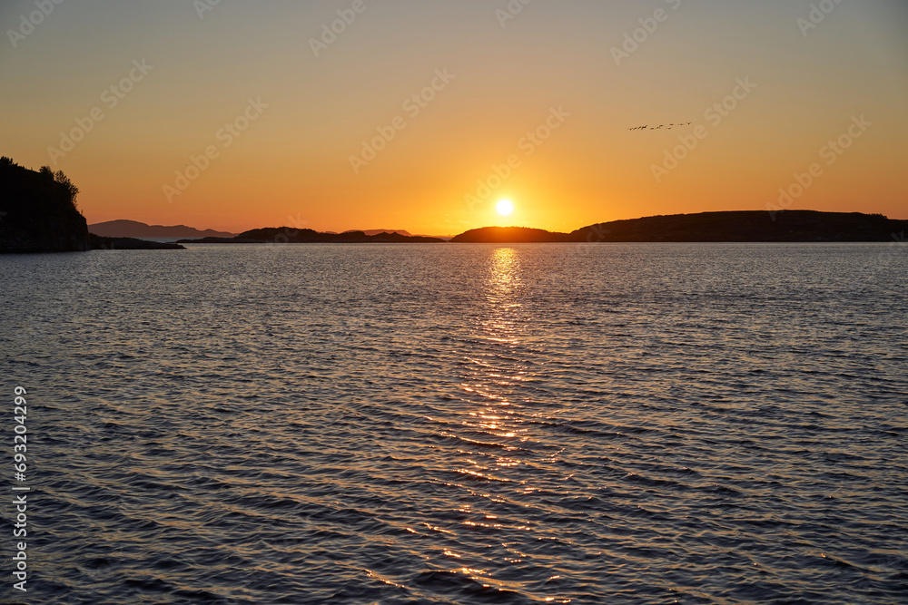 Landscape picture of the midnight sun in golden hour over the Norwegian sea with small islands at coast of northern Norway. Picture is taken from rocky beach in the arctic summer calm night.