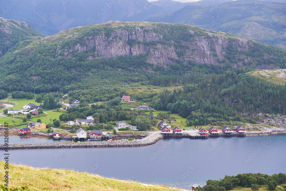Small norwegian willage under high mountain range in the fjord with typical and traditional red painted wooden fisherman houses just on the water edge. Beautiful example of scandinavian countryside.