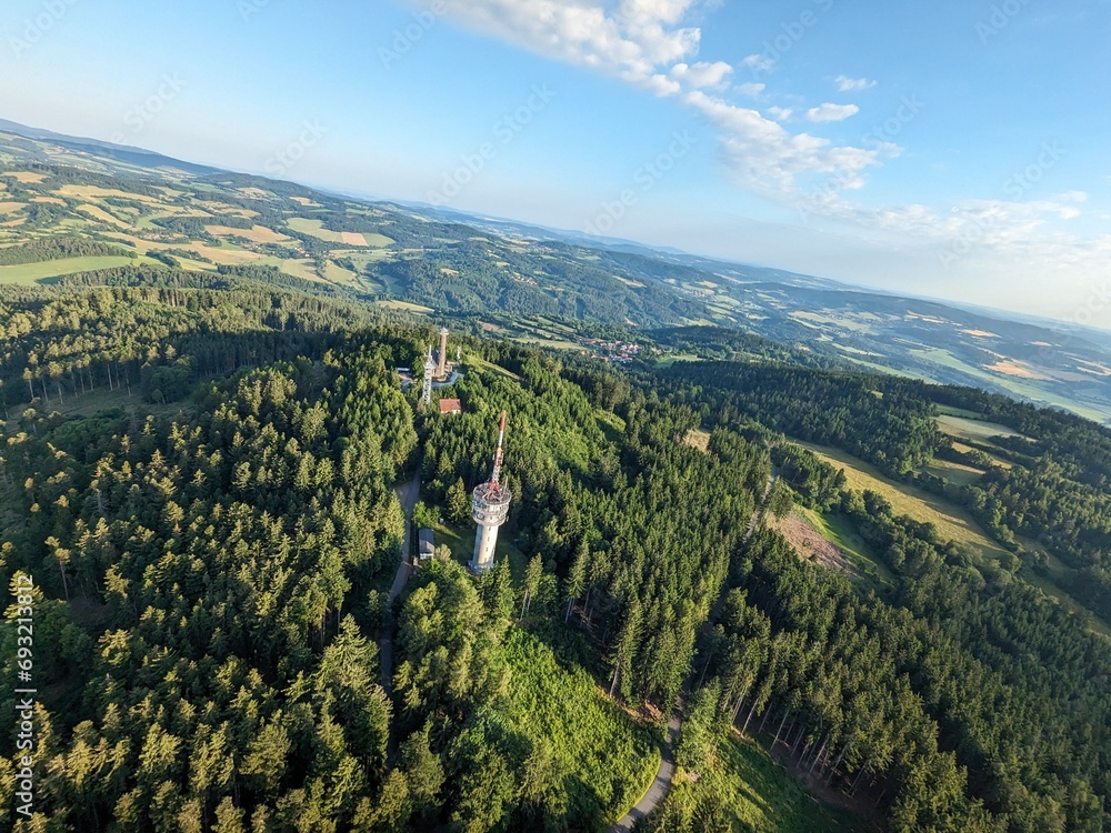 Aerial view of the top of Svatobor hill with a historic lookout tower with a tourist hut,a telecommunications tower and a TV retranslation tower.