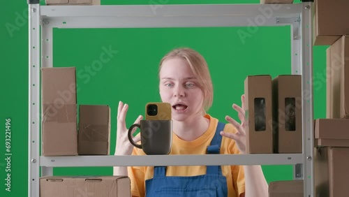 In the frame on a green background, a limp. Depicts a young woman in a uniform. Depicts an employee, in a warehouse. She is posing with a camera phone, adjusting her hair, getting all prettier