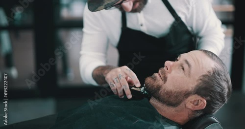 Relax, beard or shave with a barber and man in a seat as a customer for luxury or professional service. Industry, salon or hairdresser and a person grooming the face of a client with a machine photo