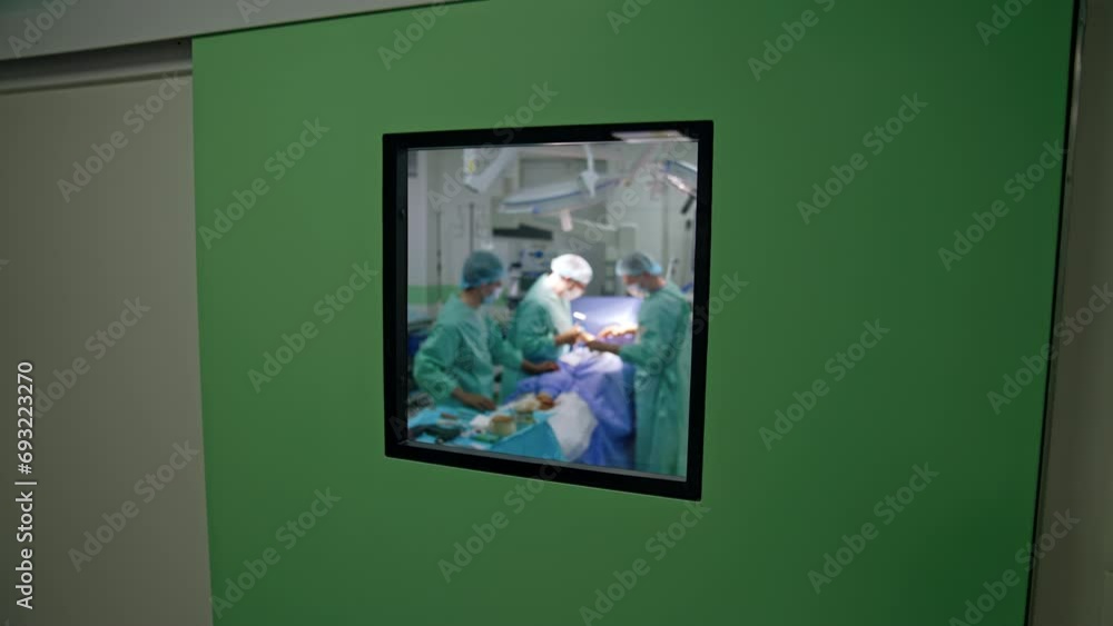 View of the surgical room through the window in the door. Team of doctors work in the operational theatre. View of the surgical room through the window in the door. Team of doctors work in the operational theatre.