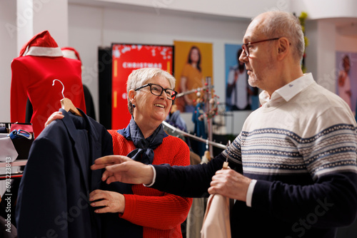 Slika na platnu Customers checking suit jacket fabric in clothing store, reviewing blazers on racks and visiting mall to buy gifts on discount