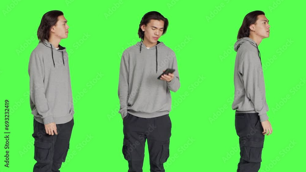 Dissatisfied guy in studio awaiting a thing, wandering about and monitoring time on wristwatch against greenscreen backdrop. Asian guy annoyed and impulsive, looks at his timepiece. Dissatisfied guy in studio awaiting a thing, wandering about and monitoring time on wristwatch against greenscreen backdrop. Asian guy annoyed and impulsive, looks at his timepiece.