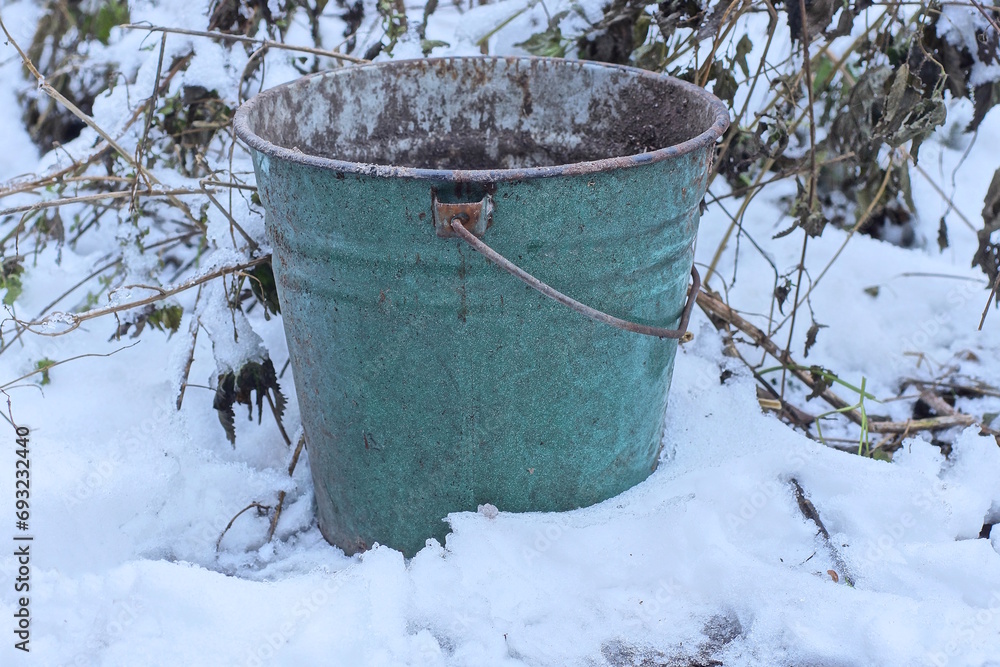 one old dirty green metal bucket stands on white snow on a winter street one old dirty green metal bucket stands on white snow on a winter street