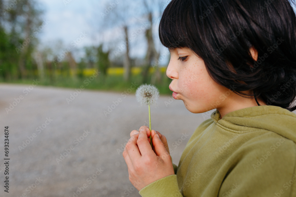side view of child with freckles in green top blowing a dandelion outdoors side view of child with freckles in green top blowing a dandelion outdoors