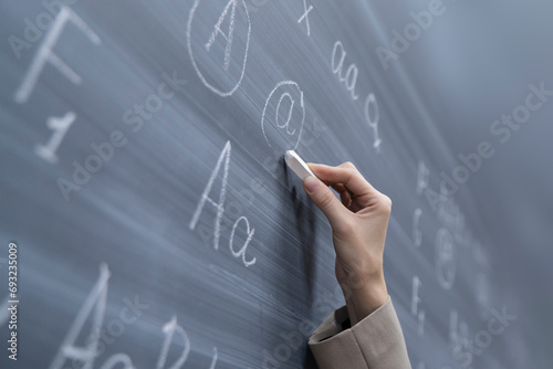 close up student's hand holding piece of chalk and writing on blackboard