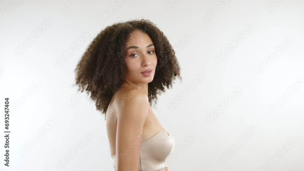 Attractive young woman with african curls, slim silk body wearing strapless bra, hugging herself gently, touching body seductively. White background. High quality 4k footage