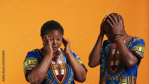 African american people suffering from migraine on camera, having flu symptoms and being exhausted in studio. Man and woman with headache rubbing temples to ease the pressure, unwell couple. photo