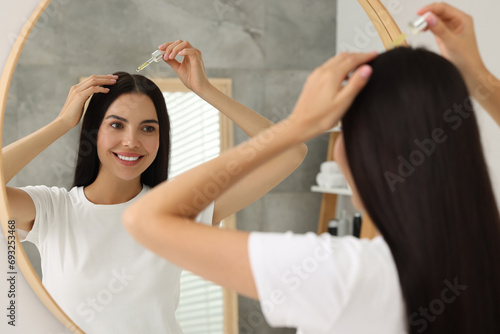 Beautiful woman applying hair serum in bathroom. Cosmetic product photo