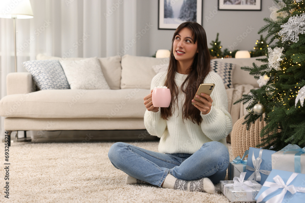 Smiling woman with cup of Christmas cocoa and smartphone at home. Space for text Smiling woman with cup of Christmas cocoa and smartphone at home. Space for text