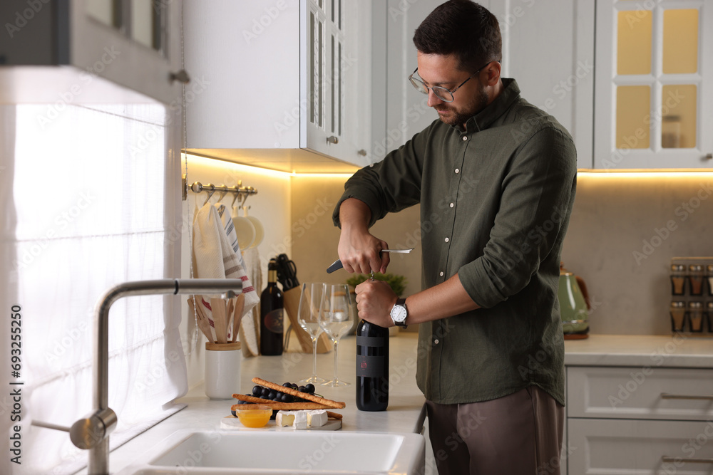 Romantic dinner. Man opening wine bottle with corkscrew at countertop in kitchen Romantic dinner. Man opening wine bottle with corkscrew at countertop in kitchen