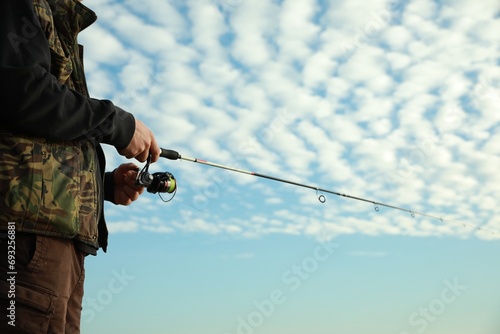 Fisherman with rod fishing under cloudy sky, closeup. Space for text