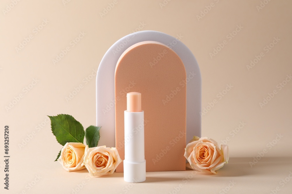 Stylish presentation of lip balm with rose flowers on beige background Stylish presentation of lip balm with rose flowers on beige background