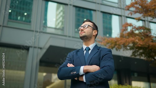 Confident business man standing in front of office building, arms crossed looking up with admiration photo
