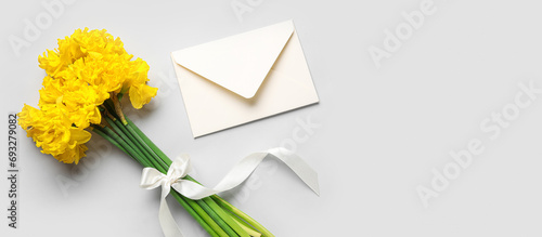 Bouquet of beautiful narcissus flowers and envelope on light background with space for text, top view photo