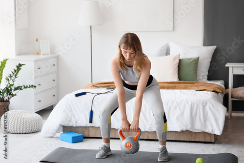 Young sporty woman training with kettlebell at home photo