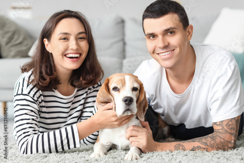 Young couple with cute Beagle dog lying on carpet at home