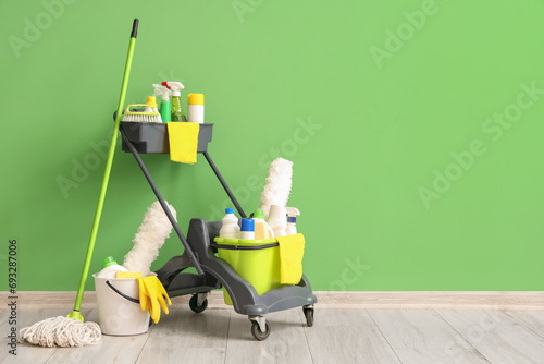Trolley with cleaning supplies near green wall