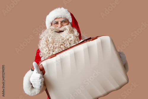 Santa Claus with suitcase showing thumb-up gesture on beige background. Christmas vacation concept