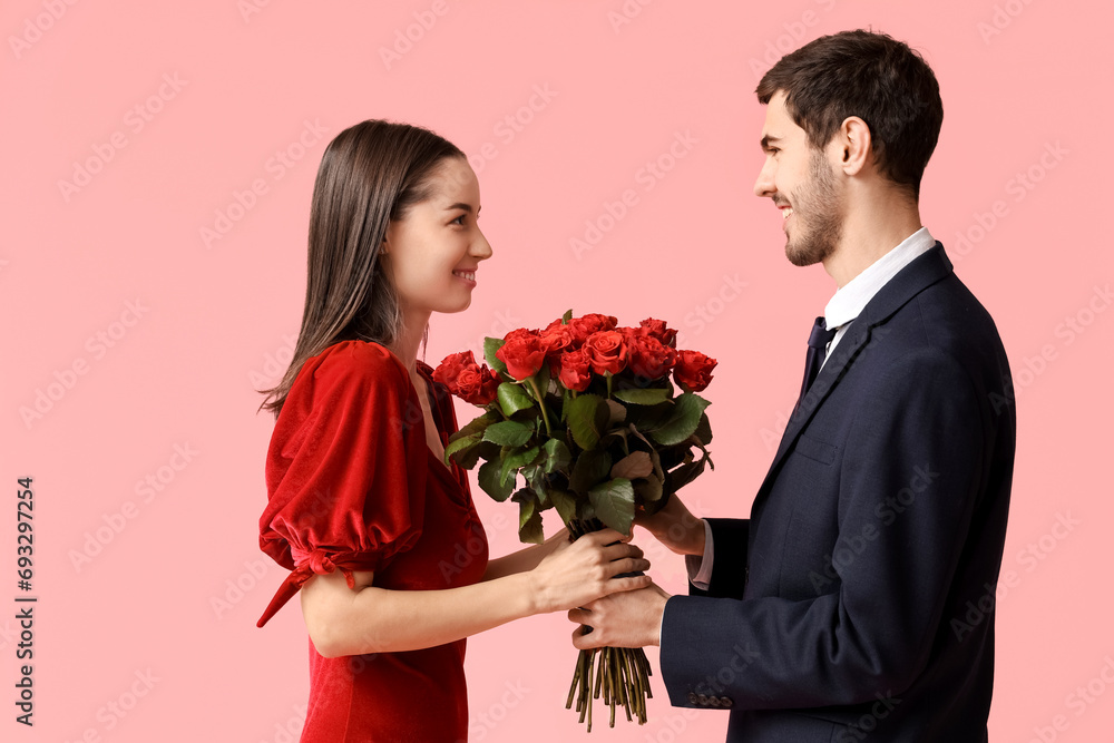 Beautiful young couple with bouquet of red roses on pink background. Valentine's day celebration Beautiful young couple with bouquet of red roses on pink background. Valentine's day celebration