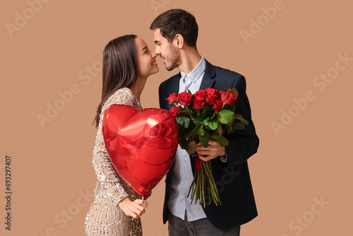 Beautiful young couple with bouquet of red roses and heart shaped air balloon on brown background. Valentine's day celebration